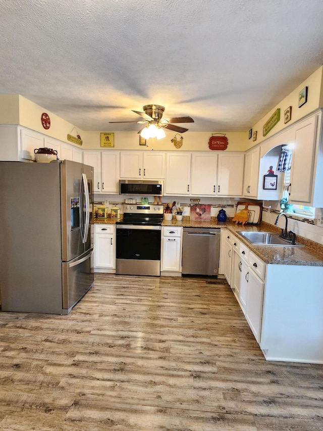 kitchen with white cabinetry, a ceiling fan, appliances with stainless steel finishes, light wood finished floors, and a sink