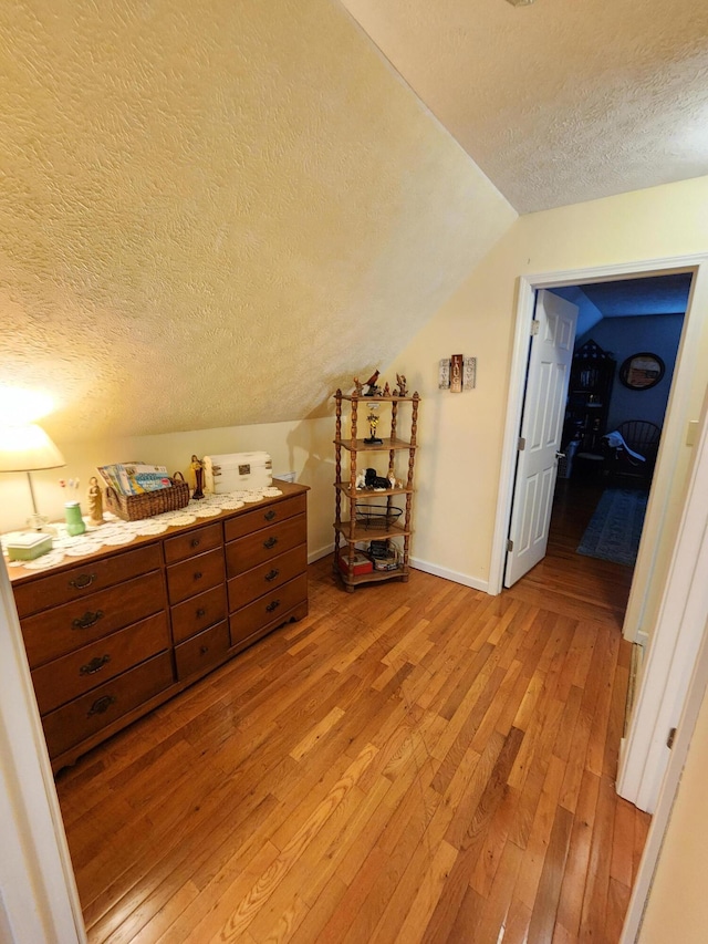 bedroom with light wood-style flooring, a textured ceiling, baseboards, and lofted ceiling