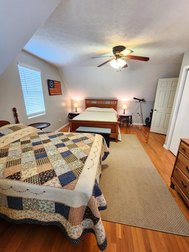 bedroom with baseboards, ceiling fan, a textured ceiling, vaulted ceiling, and wood finished floors