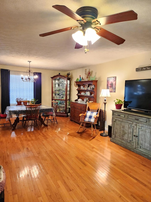 dining area featuring light wood finished floors, ceiling fan with notable chandelier, and a textured ceiling