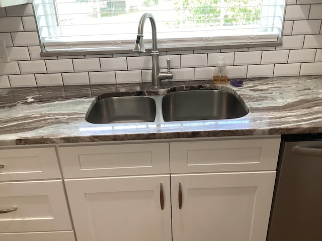 room details featuring backsplash, stainless steel dishwasher, white cabinetry, and sink