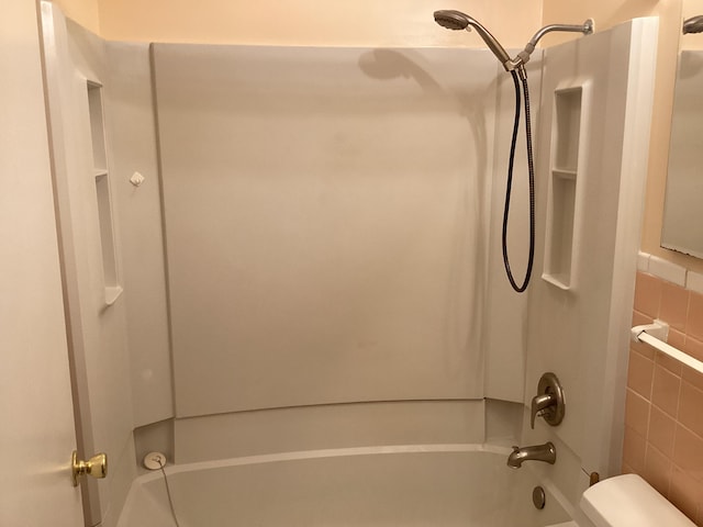 bathroom featuring shower / washtub combination, toilet, and tile walls