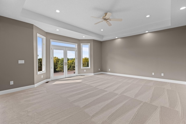 carpeted spare room with ceiling fan, french doors, and a raised ceiling