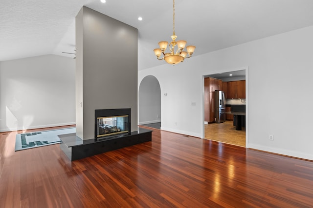 unfurnished living room featuring hardwood / wood-style flooring, a multi sided fireplace, lofted ceiling, and an inviting chandelier