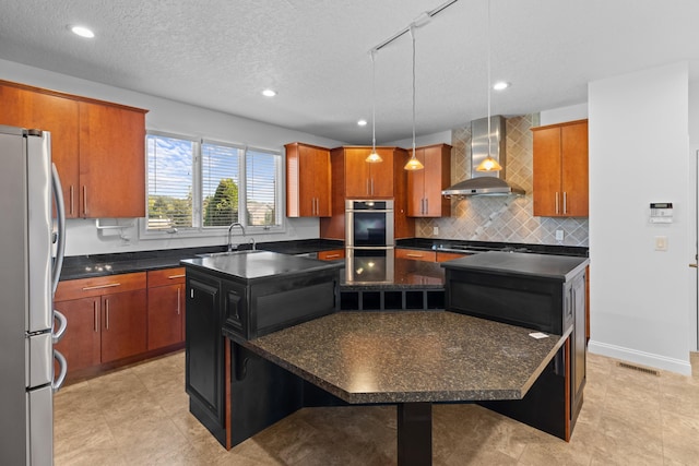 kitchen with stainless steel appliances, a kitchen island, wall chimney range hood, and decorative light fixtures