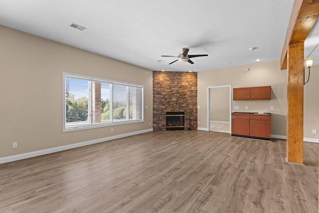 unfurnished living room featuring a fireplace, a textured ceiling, light hardwood / wood-style flooring, and ceiling fan