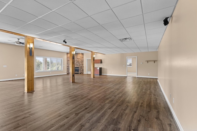 basement featuring a large fireplace, dark hardwood / wood-style floors, a drop ceiling, and ceiling fan