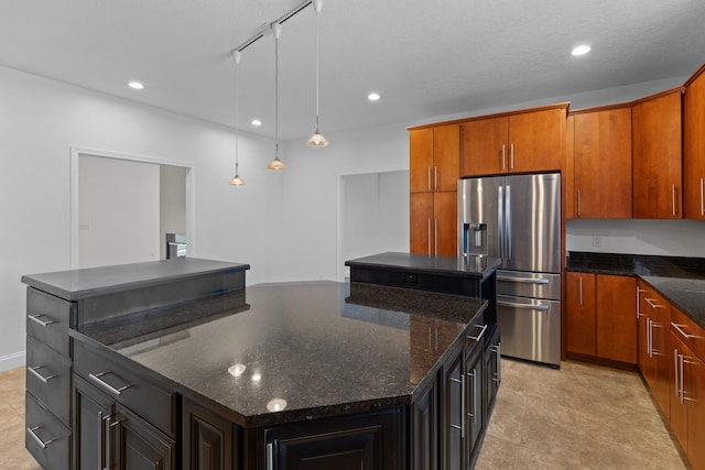 kitchen with rail lighting, stainless steel fridge with ice dispenser, hanging light fixtures, a kitchen island, and dark stone counters