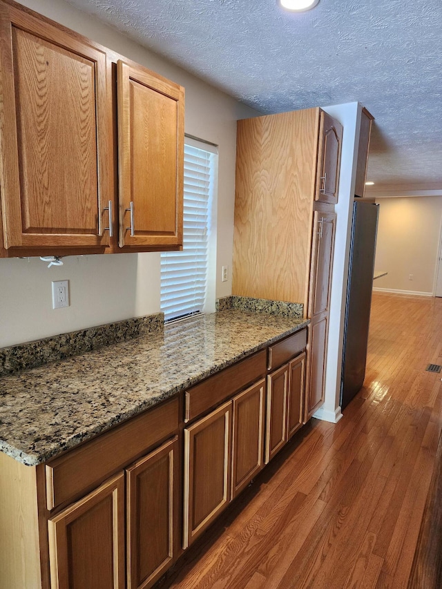 kitchen featuring stone countertops, stainless steel fridge, dark hardwood / wood-style flooring, and a textured ceiling