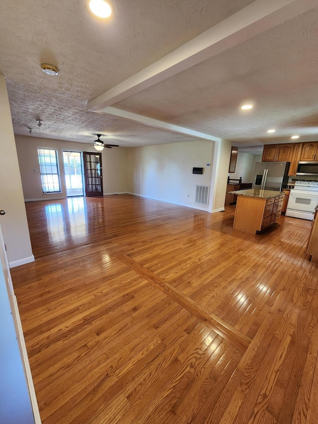 unfurnished living room featuring light wood finished floors, visible vents, baseboards, a textured ceiling, and a ceiling fan