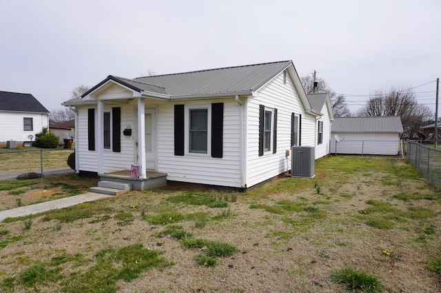 bungalow featuring metal roof, central AC, a fenced backyard, and a front lawn