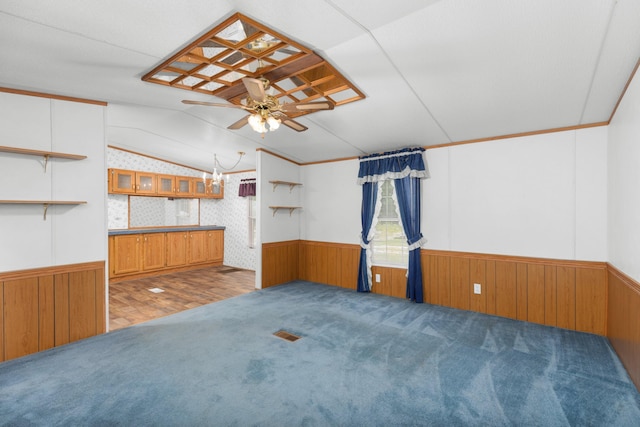 carpeted empty room featuring a wainscoted wall, ceiling fan with notable chandelier, and lofted ceiling