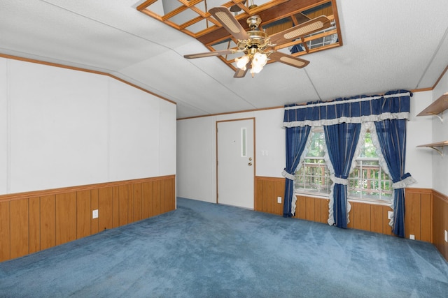 carpeted spare room with a wainscoted wall, lofted ceiling, ceiling fan, and wood walls