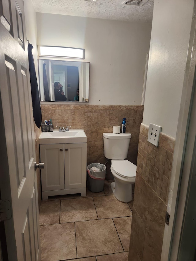 bathroom with tile walls, vanity, toilet, and a textured ceiling