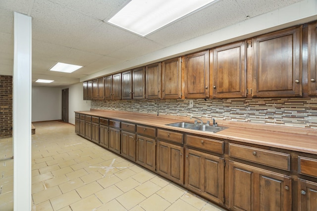 kitchen with tasteful backsplash, wooden counters, sink, and a drop ceiling