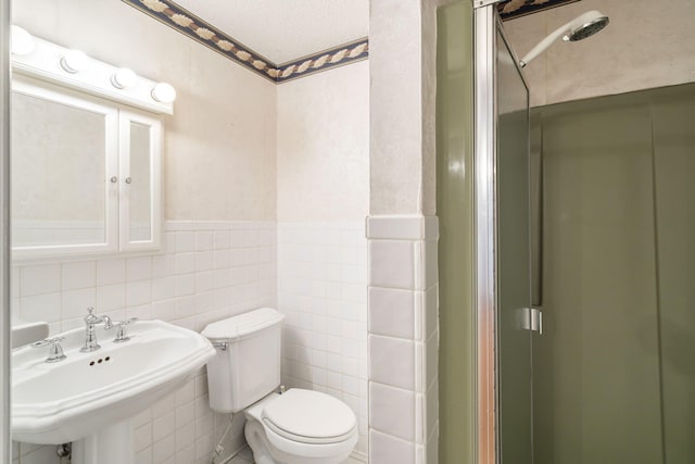 bathroom with walk in shower, toilet, sink, and tile walls