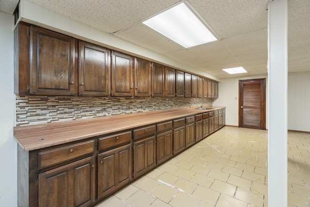 kitchen featuring dark brown cabinetry, decorative backsplash, and a paneled ceiling