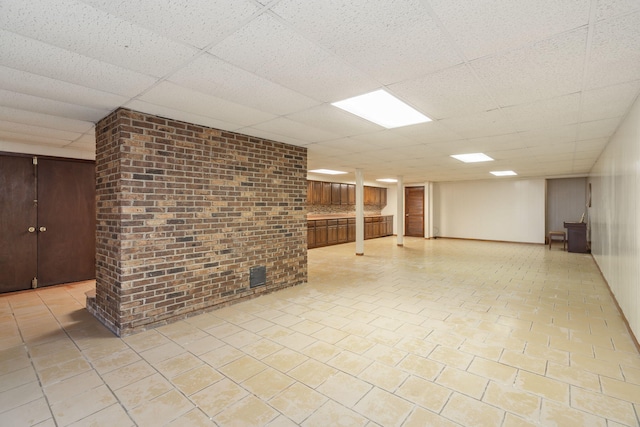 basement featuring brick wall, light tile patterned floors, and a drop ceiling