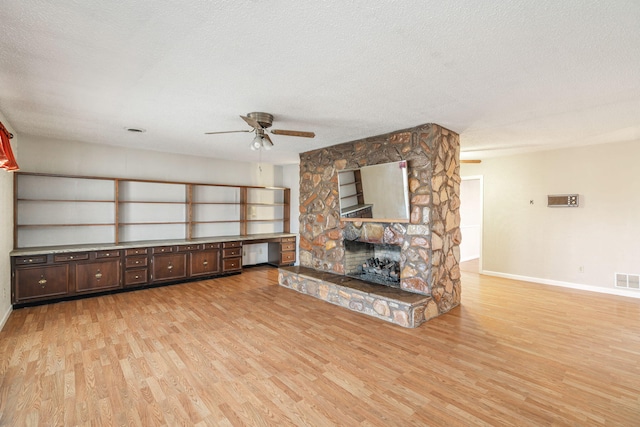 unfurnished living room with light hardwood / wood-style flooring, a fireplace, built in desk, and a textured ceiling