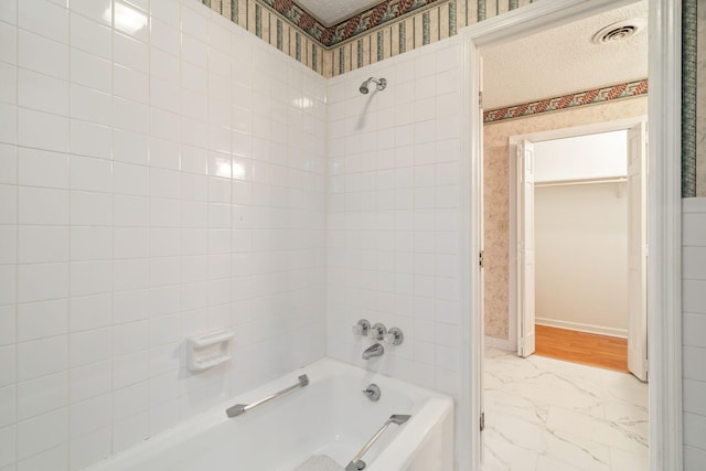 bathroom with a textured ceiling and tiled shower / bath