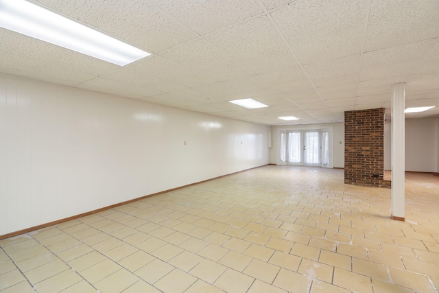 basement with light tile patterned floors, a paneled ceiling, and french doors