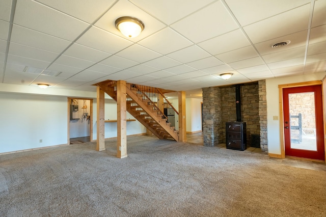 basement with carpet floors, a paneled ceiling, and a wood stove