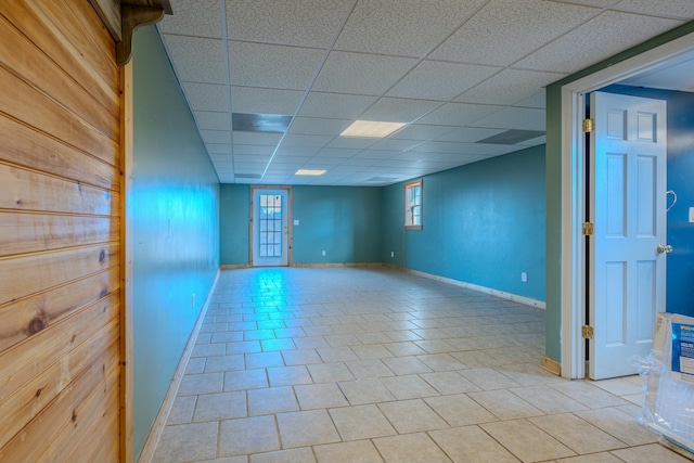 basement with a drop ceiling, light tile patterned floors, and baseboards