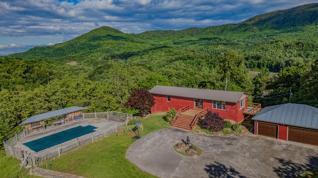 aerial view of property and surrounding area with a heavily wooded area, a mountainous background, and a pool