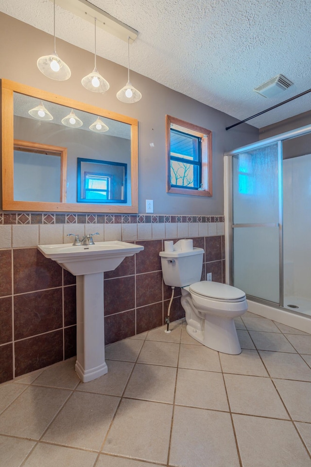 bathroom featuring tile walls, a stall shower, a textured ceiling, tile patterned flooring, and toilet