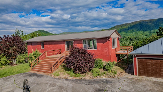 view of front facade featuring brick siding, metal roof, a deck with mountain view, a garage, and asphalt driveway