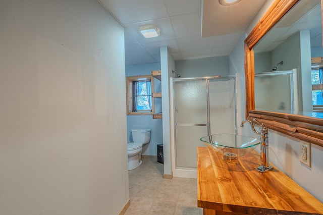 bathroom featuring walk in shower, toilet, sink, tile patterned flooring, and a drop ceiling