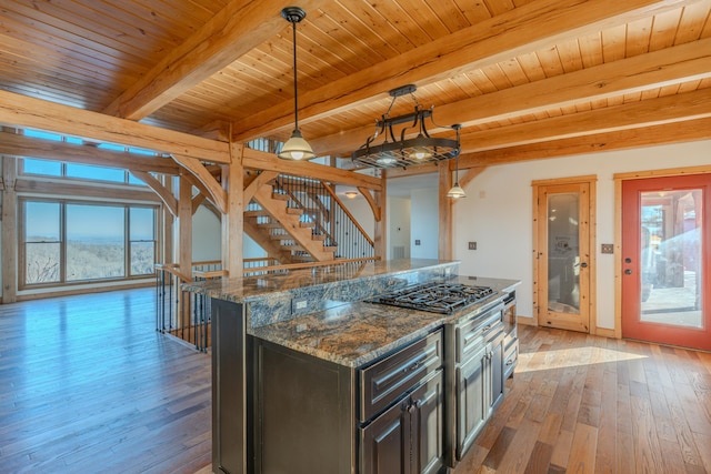 kitchen with beamed ceiling, a center island, light wood-type flooring, dark stone countertops, and pendant lighting