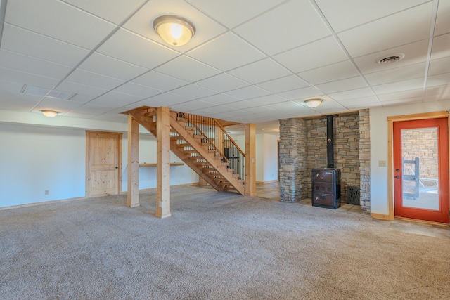 finished basement featuring stairs, carpet flooring, a drop ceiling, a wood stove, and baseboards