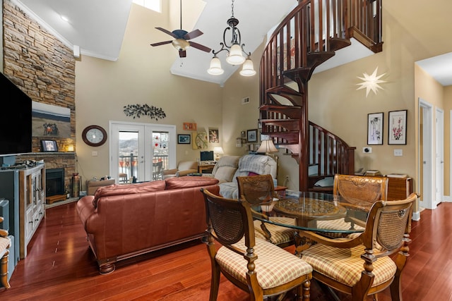 dining area with hardwood / wood-style flooring, ceiling fan, a high ceiling, a stone fireplace, and french doors