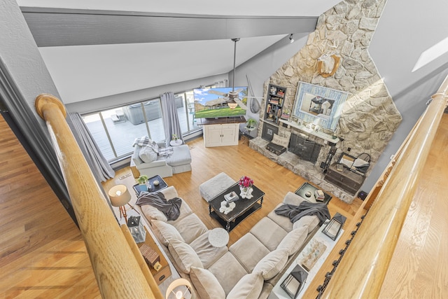 living room with a stone fireplace, wood-type flooring, and vaulted ceiling