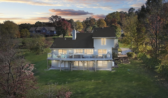 back house at dusk featuring a lawn and a wooden deck