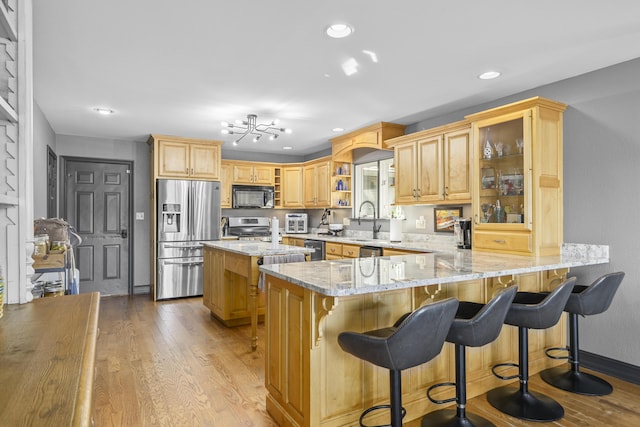 kitchen featuring light wood-type flooring, light stone counters, appliances with stainless steel finishes, a kitchen bar, and kitchen peninsula