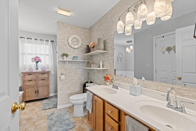 bathroom featuring vanity, brick wall, and toilet