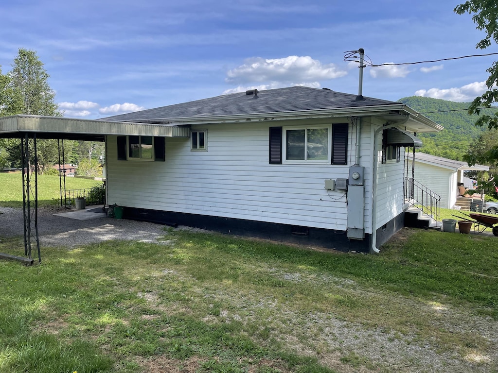 back of house with entry steps, a yard, a shingled roof, and an attached carport
