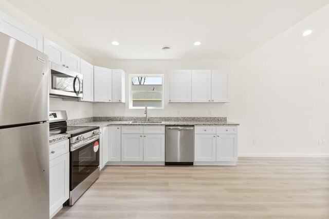 kitchen featuring light wood-style flooring, stainless steel appliances, a sink, white cabinets, and light stone countertops