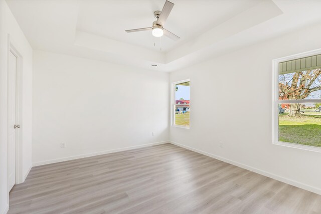 empty room featuring baseboards, a tray ceiling, and light wood finished floors