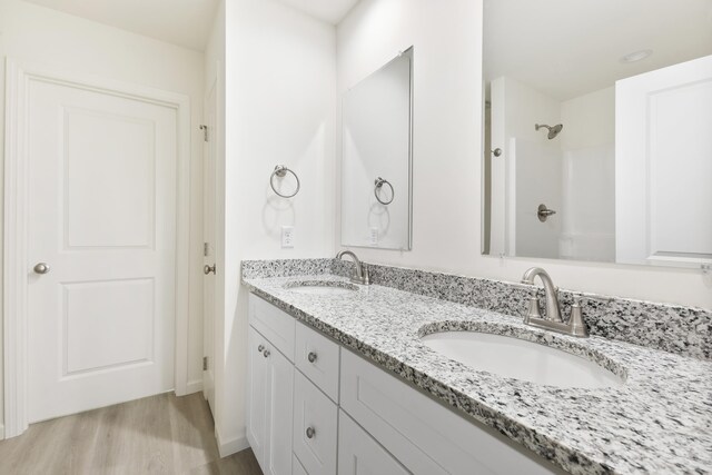 bathroom with double vanity, a sink, walk in shower, and wood finished floors
