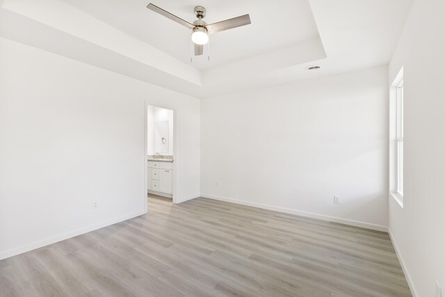 spare room featuring a tray ceiling, a healthy amount of sunlight, light wood-type flooring, baseboards, and ceiling fan