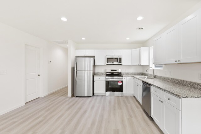 kitchen featuring light wood finished floors, white cabinets, a sink, and stainless steel appliances