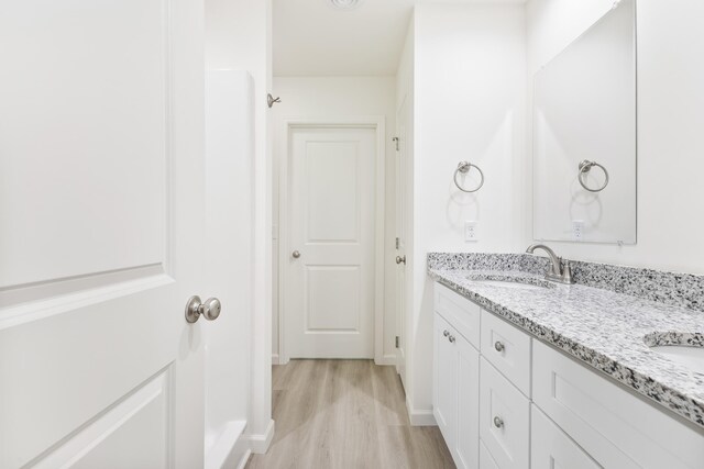 full bath with baseboards, double vanity, a sink, and wood finished floors