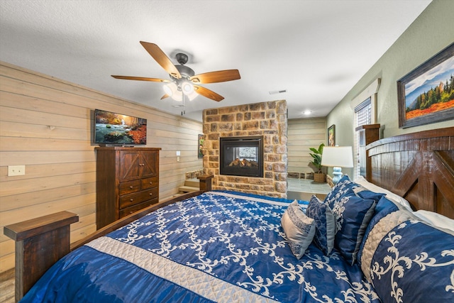 bedroom with a fireplace, ceiling fan, and wooden walls