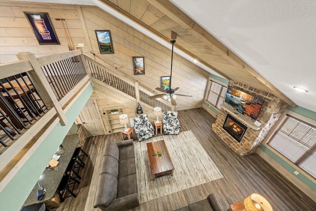 living room featuring wood walls, lofted ceiling with beams, a stone fireplace, ceiling fan, and dark hardwood / wood-style floors