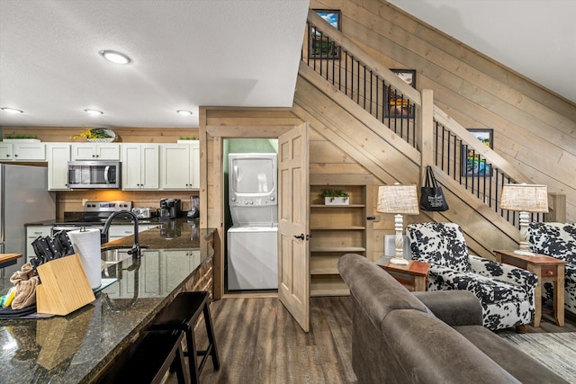 living room featuring wood walls, sink, a textured ceiling, stacked washer / drying machine, and dark hardwood / wood-style flooring