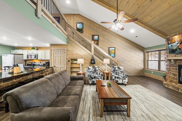 living room featuring a stone fireplace, wood walls, lofted ceiling with beams, and hardwood / wood-style flooring