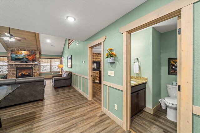 bathroom with ceiling fan, a brick fireplace, vaulted ceiling, toilet, and hardwood / wood-style flooring